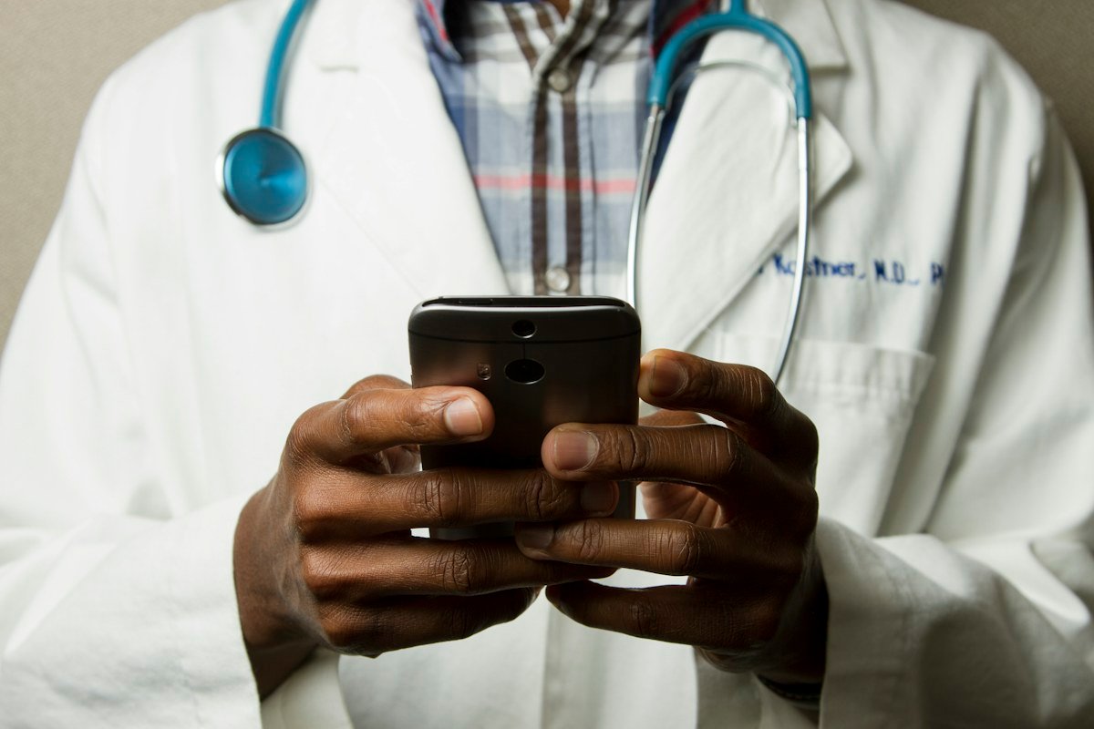 A doctor in a white coat holding a phone, stethoscope around their neck