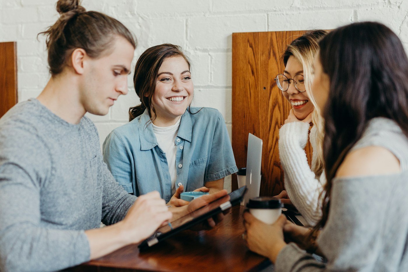 Four colleagues laughing together while reviewing work on a laptop at a wooden table