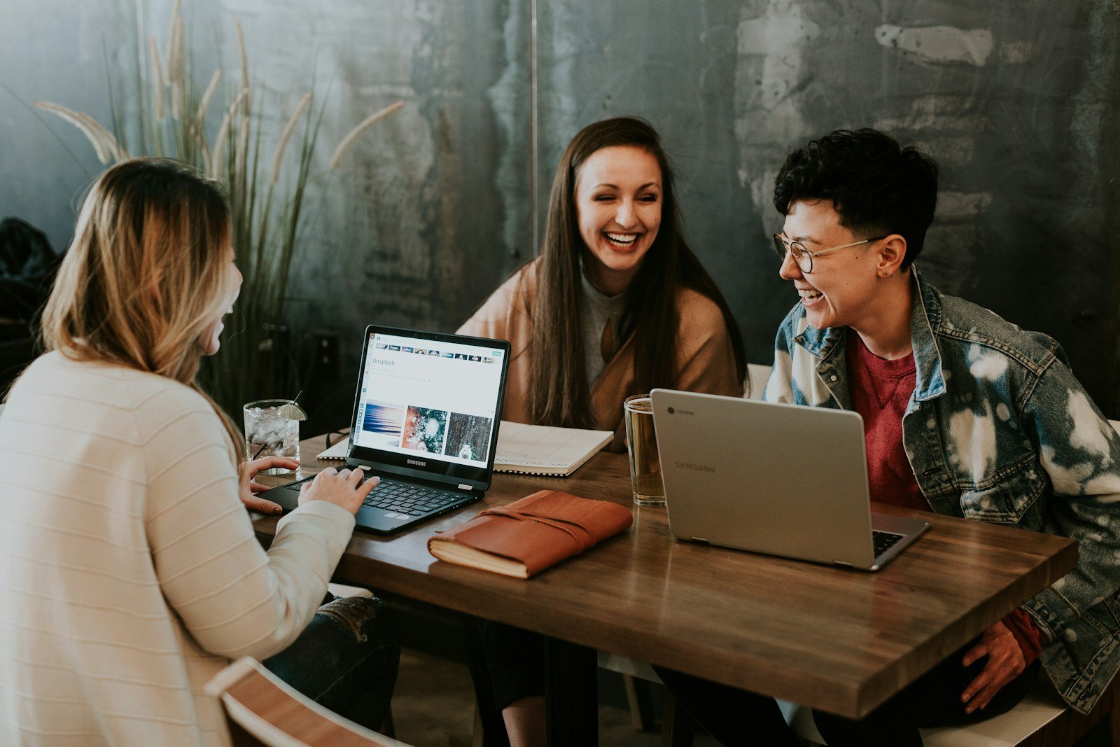 Three colleagues laughing together while reviewing work on laptops